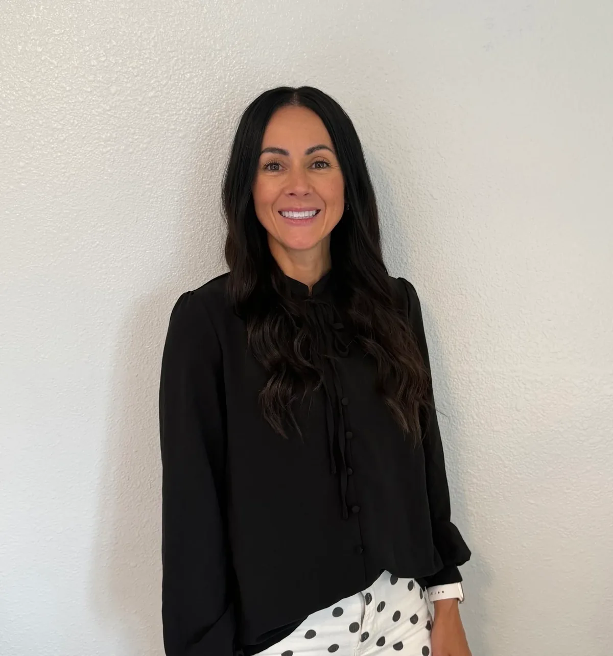 Sidney photographer Natasha Haupt, founder of 308 Sports Media, smiling in a black blouse against a white wall.