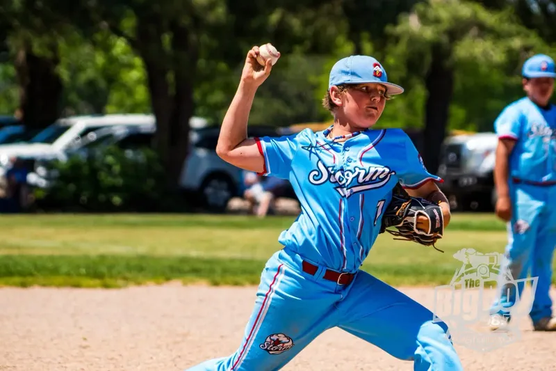 Youth baseball pitcher in a light blue Storm uniform delivering a pitch during a summer game in Sidney, Nebraska