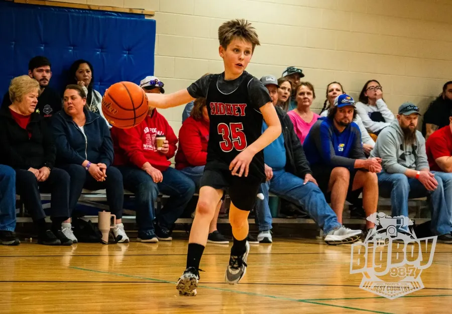 Youth basketball player in a Sidney jersey dribbling up the court in front of a full crowd at The Center