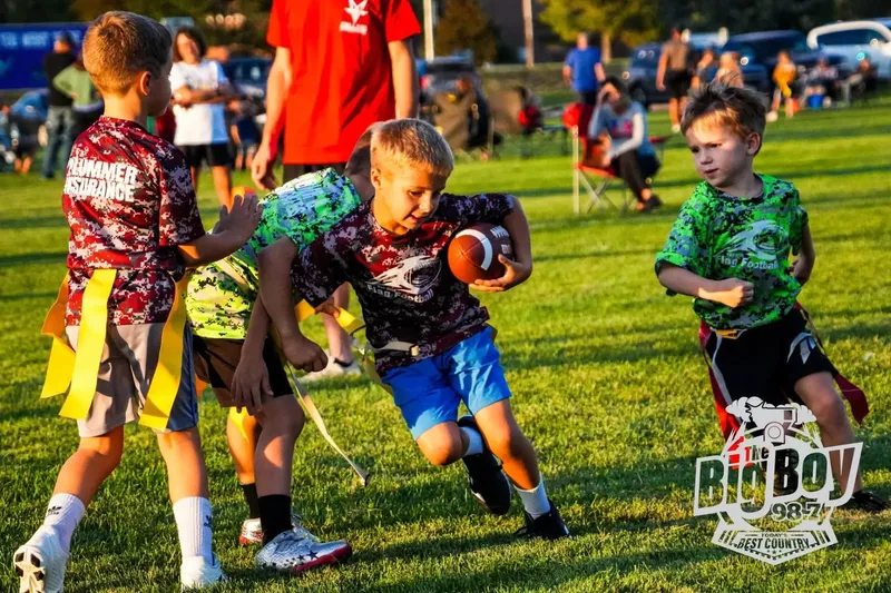 Youth flag football player carrying the ball past defenders during an evening game in Sidney, Nebraska
